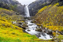 Ein Wasserfall über einer felsigen Landschaft mit einem Fluss, der sich über die Felsen ergießt; Djupivogur, östliche Region, Island — Stockfoto