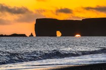 Reynisfjara, formazioni rocciose di basalto al largo della costa, e una spiaggia di sabbia nera al tramonto; Myrdalshreppur, Regione meridionale, Islanda — Foto stock