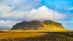 Affleurement accidenté recouvert de toundra verte avec une route traversant le vaste paysage ; Islande — Photo de stock