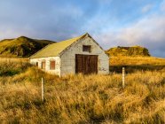 Capannone stagionato in un'area erbosa con recinzione di filo e affioramenti rocciosi sullo sfondo; Islanda — Foto stock