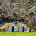 Due case indentiche con porte blu e tetti erbosi costruiti nella roccia di un fianco della montagna; Rangarping eystra, Regione meridionale, Islanda — Foto stock