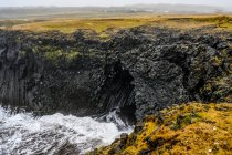 Miradouro de um penhasco para as ondas que rolam em uma caverna vulcânica ao longo da costa em Arnarstapi; Snaefellsbaer, região ocidental, Islândia — Fotografia de Stock