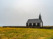 Edificio de la iglesia con campanario y cruz en una zona remota con muro de piedra y hierba; Snaefellsbaer, Región occidental, Islandia - foto de stock