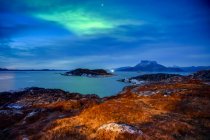 Die Nacht bricht über die zerklüftete Küste Grönlands herein, mit einem grünen Leuchten am Himmel, das sich im ruhigen Wasser darunter widerspiegelt; Nuuk, Sermersooq, Grönland — Stockfoto