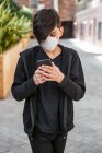 Garçon utilisant son téléphone intelligent et portant un masque de protection contre la COVID-19 pendant la pandémie mondiale de coronavirus ; Toronto, Ontario, Canada — Photo de stock