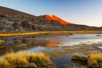 Petit lac désertique au coucher du soleil avec montagne éclairée en rouge au loin reflétant dans le lac ; San Pedro de Atacama, Atacama, Chili — Photo de stock