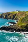 Faro bianco in cima a campi verdi collinari incorniciati da affioramenti rocciosi e cielo blu; Contea di Cornovaglia, Inghilterra — Foto stock
