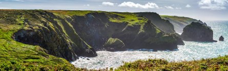 Panorama of rocky cliff shoreline with grassy fields and blue sky with clouds; Cornwall County, England — Stock Photo
