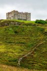 A stone castle on top of a hill covered by shrubs and a stone wall; Cornwall County, England — Stock Photo