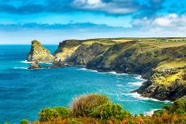 Falaises rocheuses le long du rivage avec prairies herbeuses, ciel bleu et nuages ; comté de Cornwall, Angleterre — Photo de stock