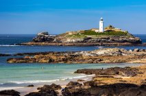 White Godrevy Lighthouse on rock formation in blue water with blue sky and rocky shoreline, Godrevy Island in St. Ives Bay; Cornwall County, England — Stock Photo