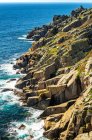 Rocky cliffs along the shoreline with surf and blue sky; Cornwall County, England — Stock Photo