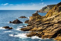 Rocky cliff formations along the shoreline with blue sky and clouds; Cornwall County, England — Stock Photo