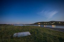 Pequeno barco branco por rio com pequena aldeia na margem do rio oposta tomada à noite com estrelas no céu; Aughinish, County Clare, Irlanda — Fotografia de Stock