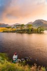 Canoë sur la rive d'un lac pointant vers une île avec des pins avec un lever de soleil épique en arrière-plan ; Connemara, comté de Galway, Irlande — Photo de stock
