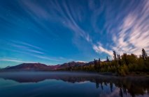 Streaks of clouds over Beach Lake at night, Chugach Mountains and autumn coloured woods in the background, South-central Alaska in autumn; Chugiak, Alaska, United States of America — Stock Photo