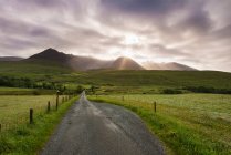 Blick auf eine Straße am frühen Morgen mit der aufgehenden Sonne hinter dem Black Cuillin Ridge; Glen Brittle, Skye, Schottland — Stockfoto