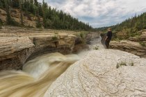 Человек, наблюдающий, как река Форель течет над водопадом Уиттакер вдоль шоссе Маккензи; Северо-Западные территории, Канада — стоковое фото