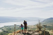 Отец со своими дочерьми, стоящими на скале с видом на озеро Оканаган; Пичленд, Британская Колумбия, Канада — стоковое фото