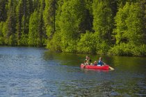 Пара и молодая девушка в красном каноэ на озере Байерс с зеленой лесной береговой линией в лагере Байерс-Лейк, Денали государственный парк; Аляска, Соединенные Штаты Америки — стоковое фото