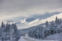 Nuages s'éclaircissant au-dessus de l'autoroute sous le vent depuis les montagnes Kenai au-dessus du col Turnagain après une tempête de neige hivernale, Neige fraîche dans les arbres, Soleil tôt le matin, Col Turnagain, Forêt nationale de Chugach, Centre-sud de l'Alaska, États-Unis. — Photo de stock