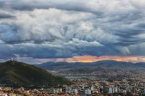 Cielo tornando tormentoso sobre el cielo de Cochabamba, con El Cristo visto en la montaña en medio de la ciudad; Bolivia - foto de stock