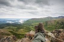 Pov de pernas de caminhante e pés descansando e desfrutando da vista da montanha plana com vista para a tigela de ancoragem, no centro-sul do Alasca, verão — Fotografia de Stock