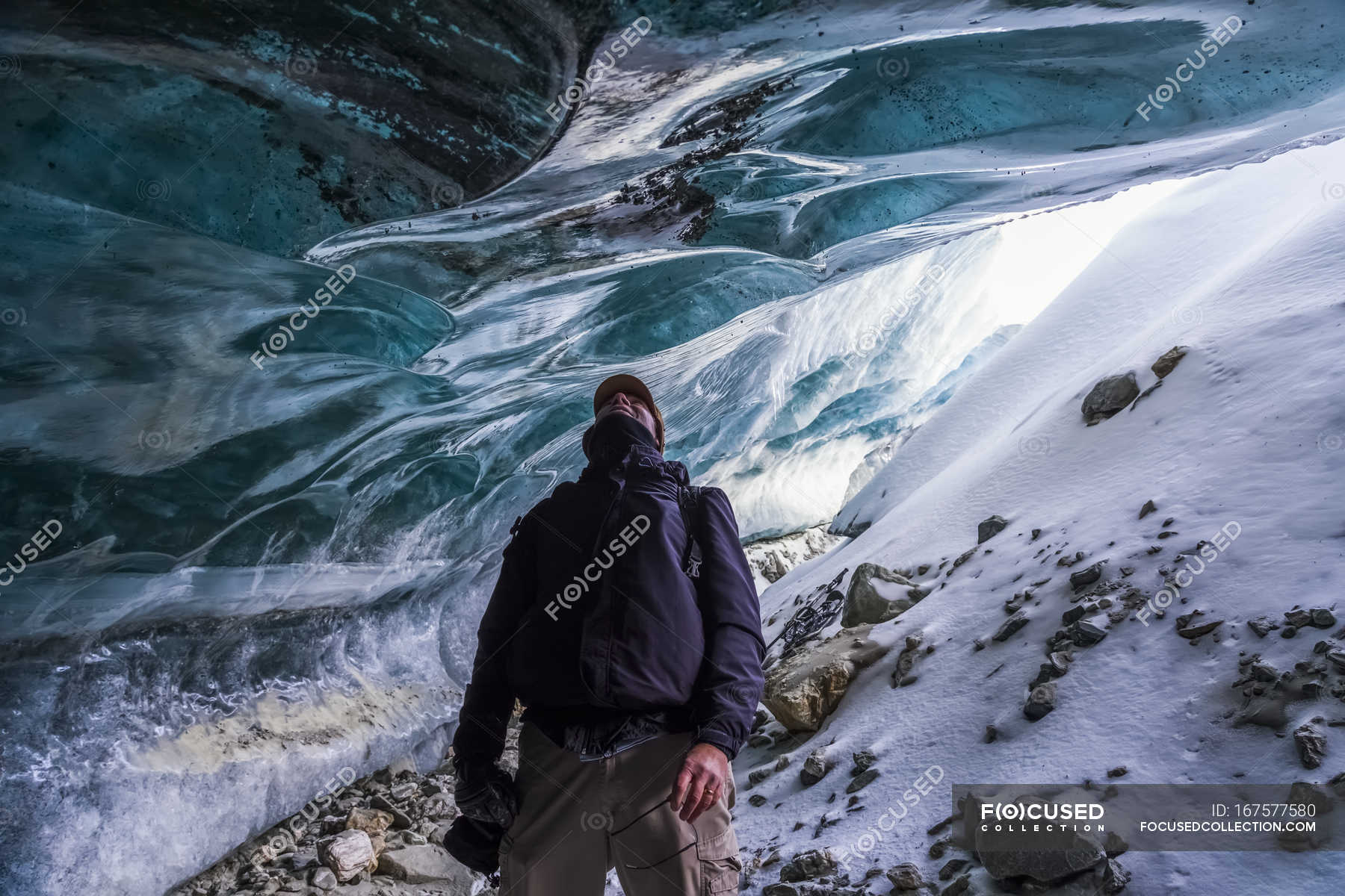 A man looks up at ice of Canwell Glacier while standing in entrance to