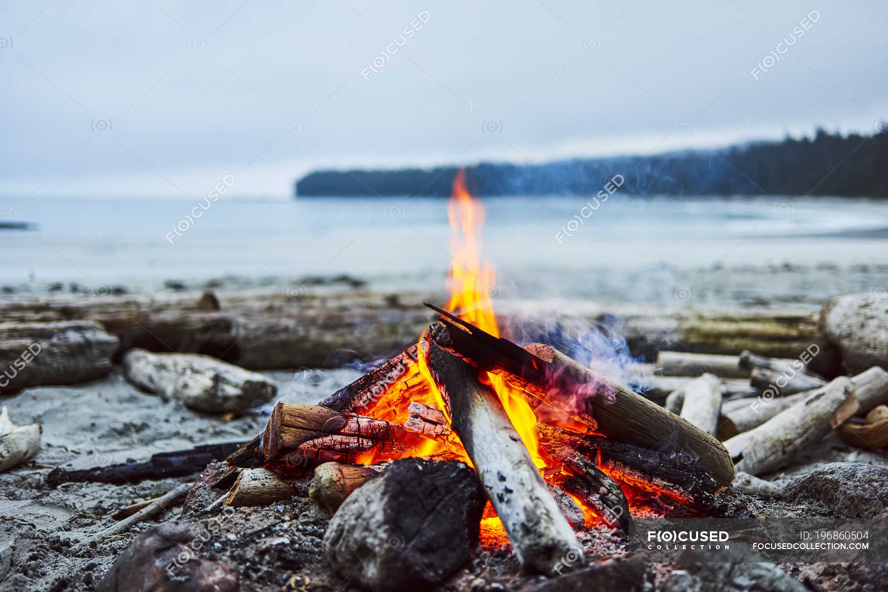 A Fire On The Beach With The Ocean And Coastline In The Background 