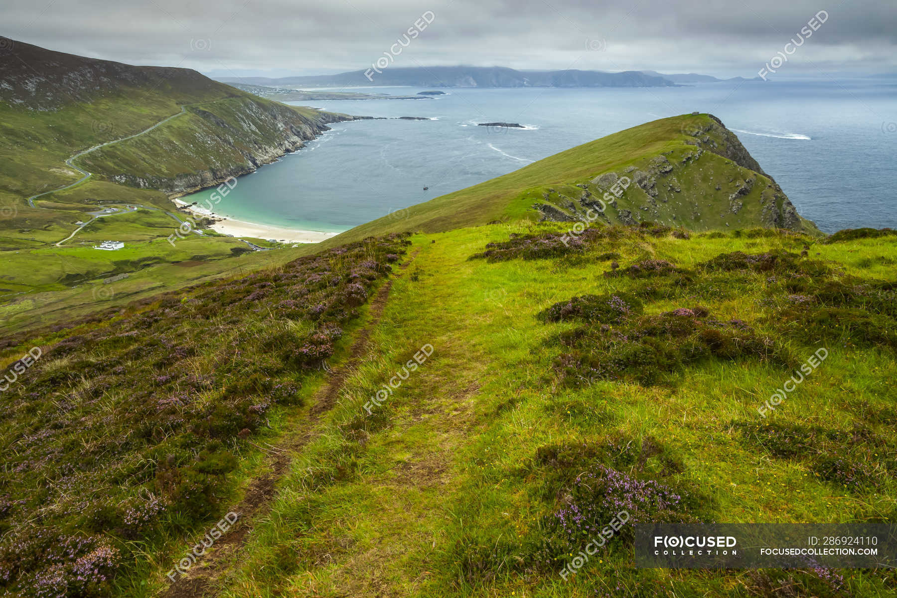 Lush grassy hills and a beach along the coast of Ireland; Ireland — sky