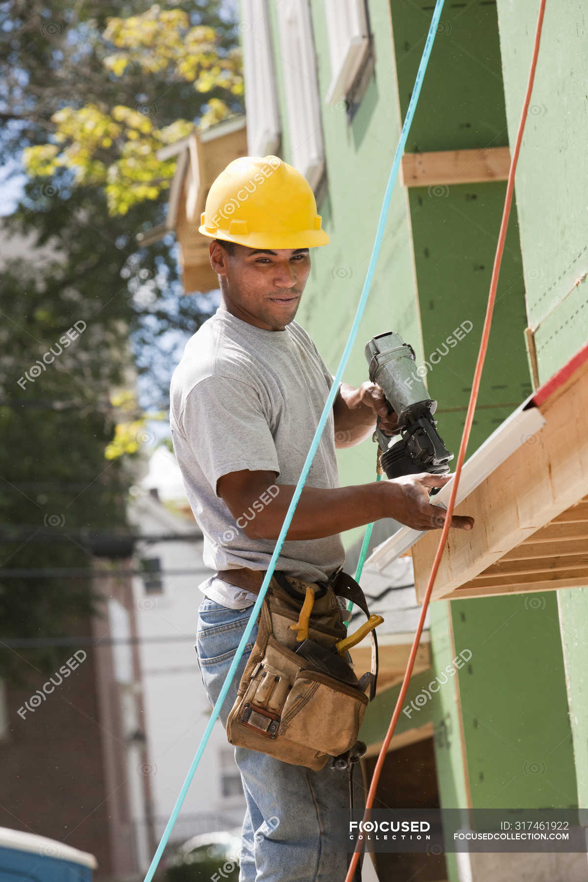 Carpenter using nail gun on edging of new house — male, Tool Belt