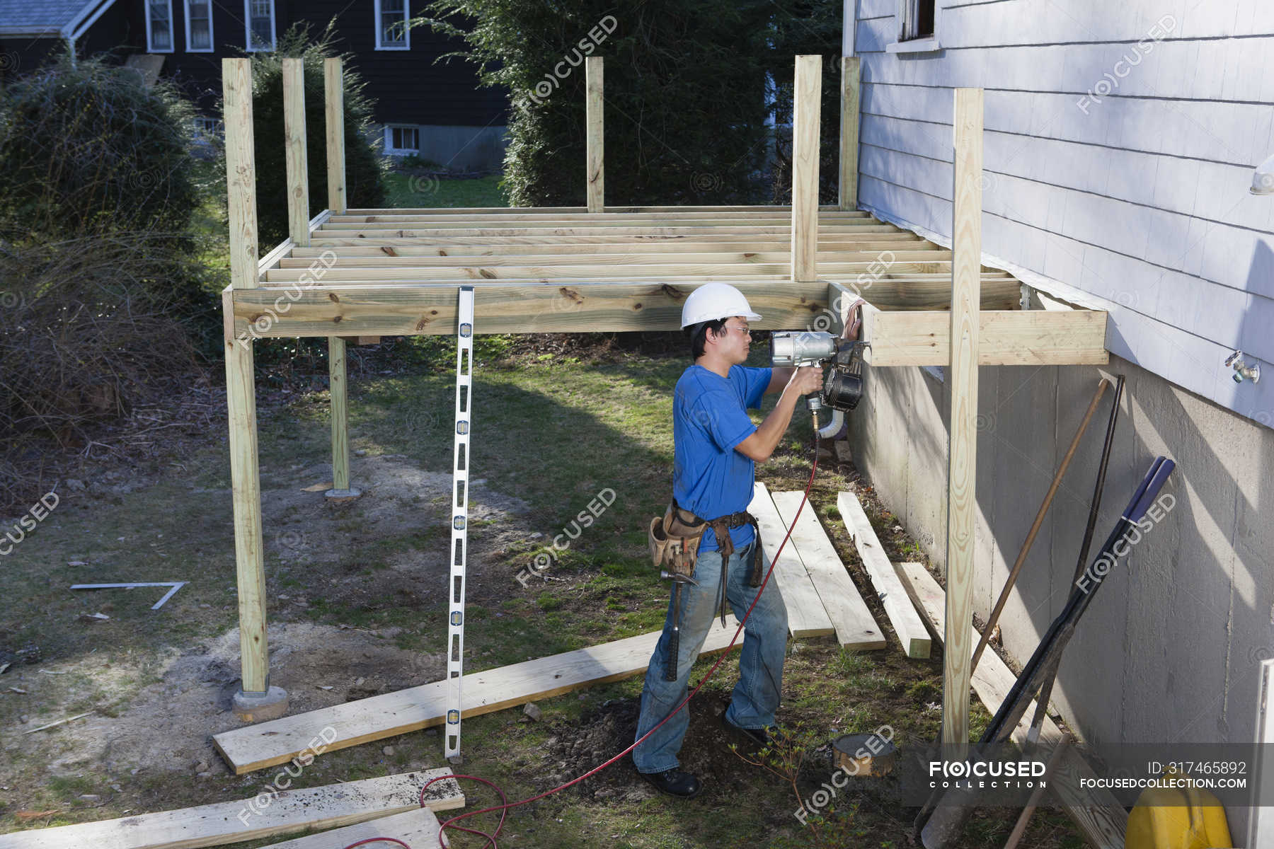 Carpenter using nail gun to install deck joists on home — male