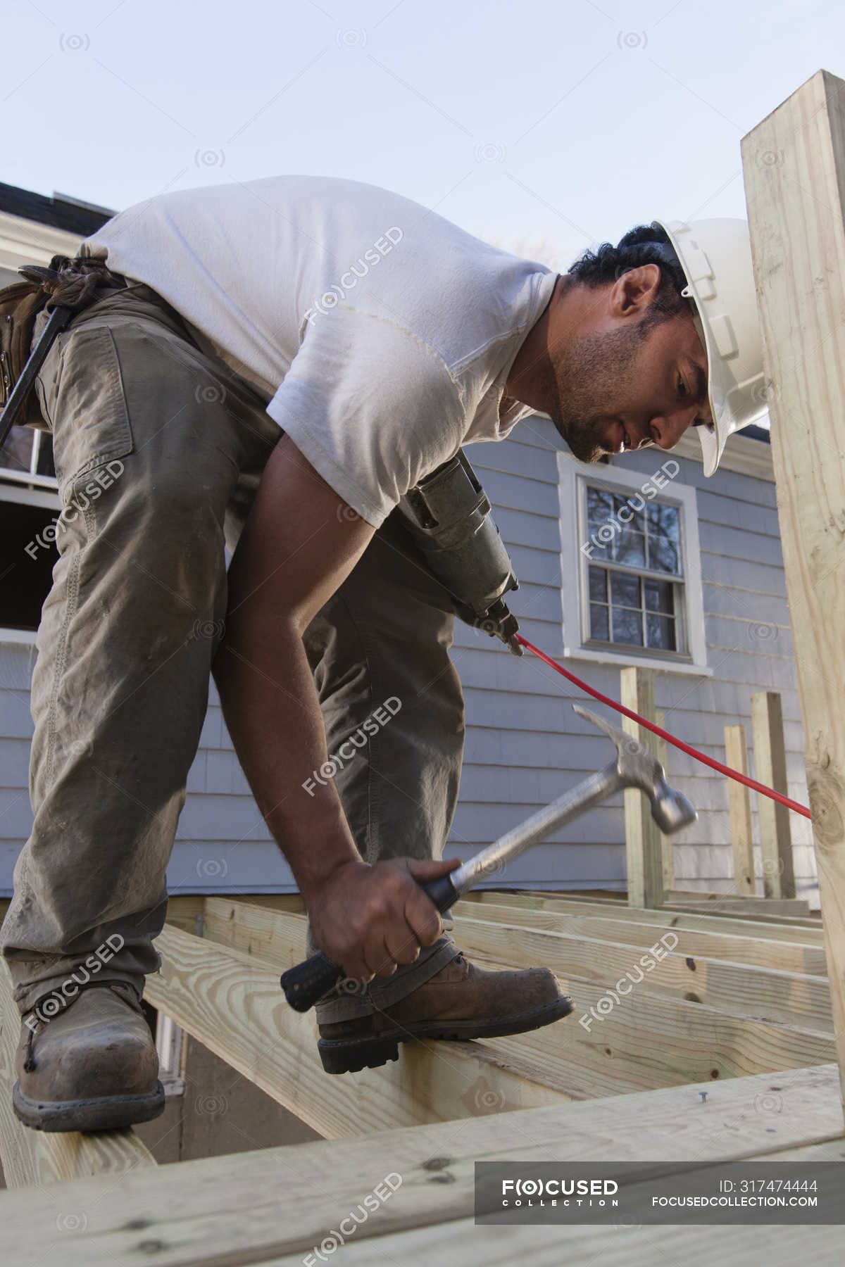 Hispanic carpenter standing on deck joists to hammer nail into decking