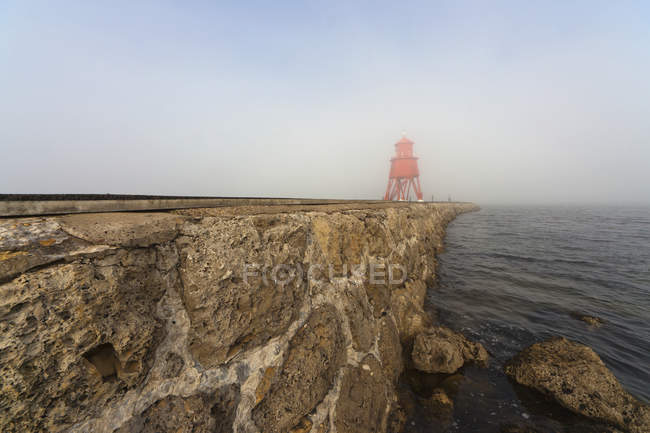 Red lighthouse in fog on coast — Stock Photo