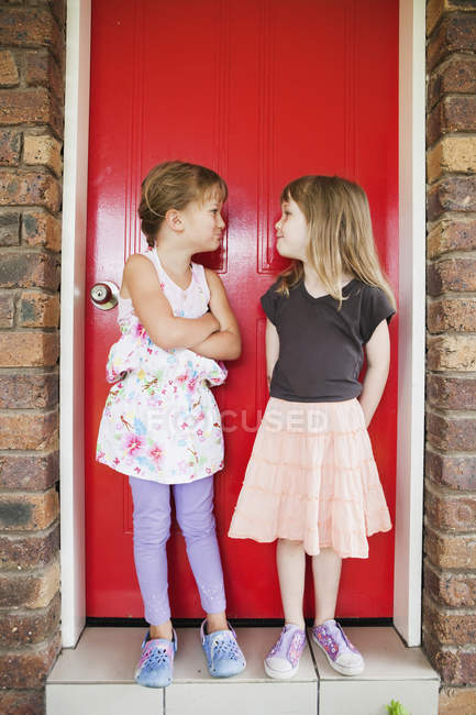 Duas meninas em pé na frente de uma porta vermelha fazendo expressões bobas uma na outra; Costa de ouro Queensland austrália — Fotografia de Stock