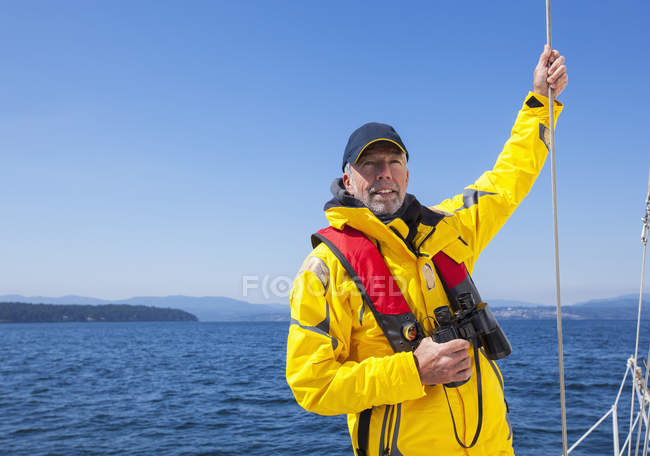 Un uomo anziano con binocolo guarda oltre le isole del Golfo mentre naviga vicino all'isola di Vancouver; British Columbia, Canada — Foto stock