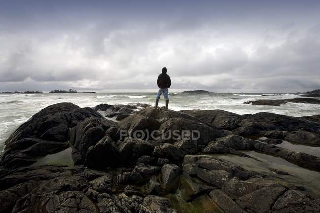 Homem de pé sobre pedras contra a água — Fotografia de Stock