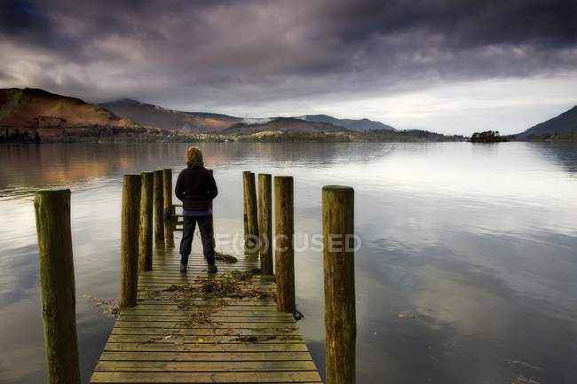 Una mujer de pie en un muelle de madera, Lago Derwent, Cumbria, Englan - foto de stock