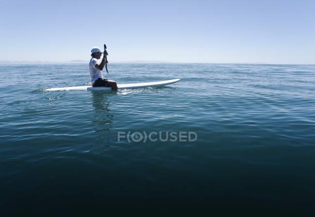 Вид сбоку на человека, сидящего на доске для серфинга — стоковое фото