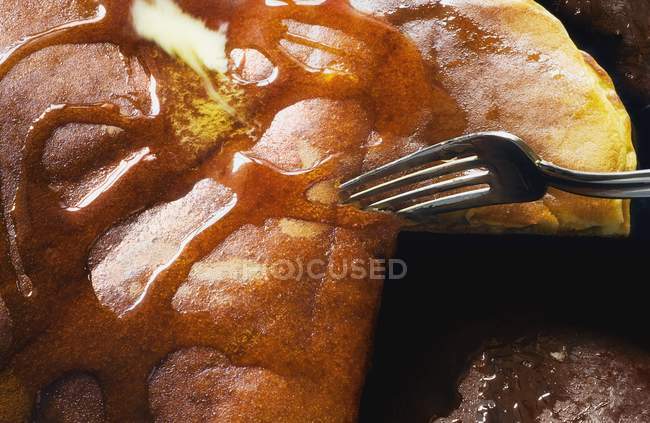 Closeup fork cutting into pancake with maple syrup — Stock Photo