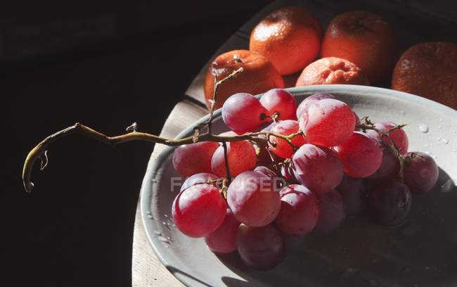 Uvas rojas en plato con mandarinas - foto de stock