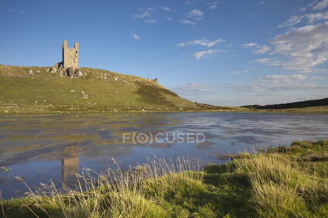 Castillo de Dunstanburgh en colina verde - foto de stock