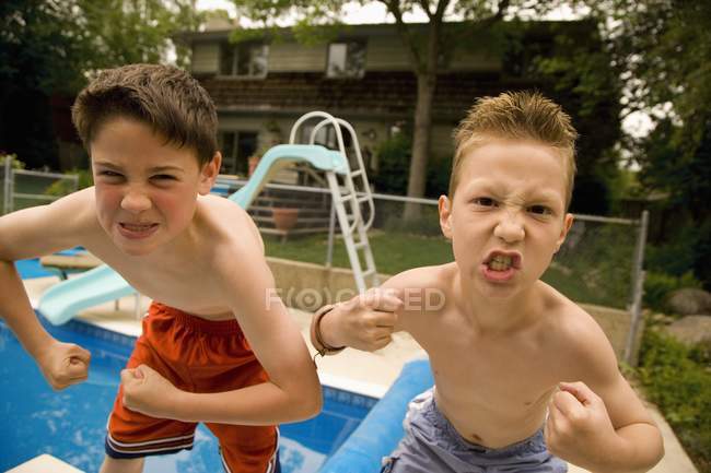 Two young boys showing muscles against pool in back yard — Stock Photo