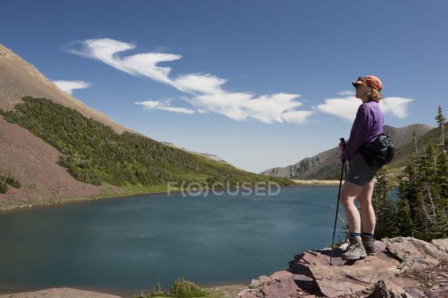 Escursionista femminile che si affaccia su un lago mentre in piedi su una scogliera rocciosa ; — Foto stock