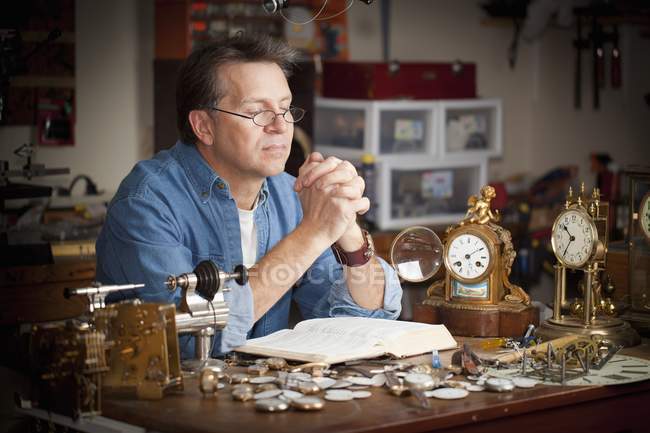 Ein Uhrmacher betet an seinem Schreibtisch in seinem Geschäft — Stockfoto