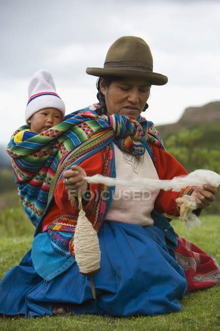 Cuzco, Pérou, Femme filant de la laine d'alpaga tout en portant bébé sur le dos — Photo de stock