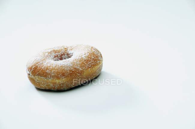 Donut dulce con azúcar en polvo que pone en la superficie blanca - foto de stock
