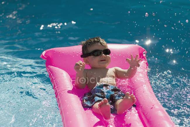 Bebê legal com óculos de sol na piscina no colchão — Fotografia de Stock