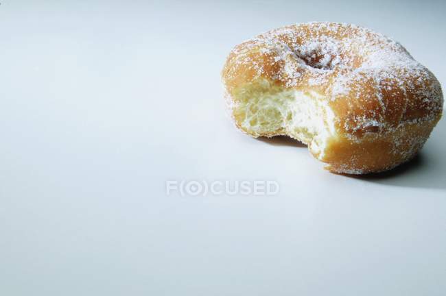 Sweet Donut partialy biten with sugar powder laying on white surface — Stock Photo