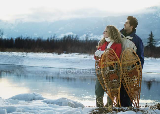 Casal com sapatos de neve em pé contra o lago — Fotografia de Stock